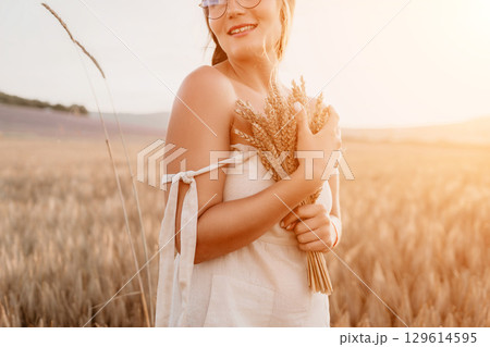 Woman wheat field. Agronomist, Woman farmer check golden ripe barley spikes in cultivated field. A woman is holding a bunch of wheat in her arms. 129614595