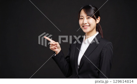 黒背景に笑顔の女性ビジネスパーソンが両手で横を指差すポーズ 129614814