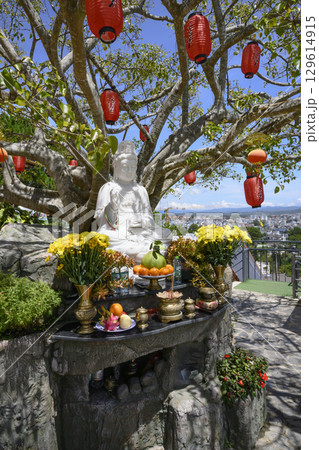Marble sculpture of a seated Buddha under a tree with paper lanterns on a hill above the city Marble sculpture of a seated Buddha under a tree with paper lanterns on a hill above the city 129614915