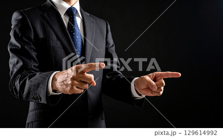 黒背景にスーツ姿の中年男性が両手で前を指差す構図 黒背景にスーツ姿の中年男性が両手で前を指差す構図 129614992