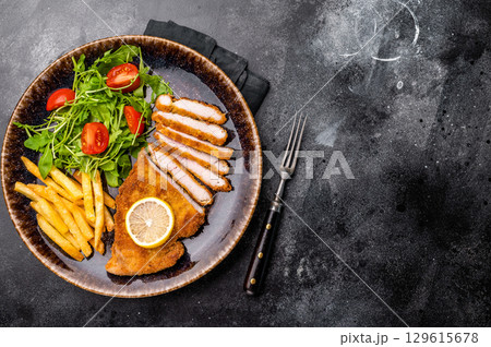 Roast viennese schnitzel steak, breaded meat with salad and french fry on a plate. black background. top view Roast viennese schnitzel steak, breaded meat with salad and french fry on a plate. black background. top view 129615678