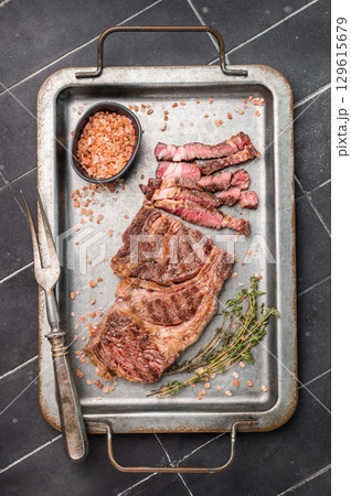 Grilled and sliced Chuck eye roll steak in a steel tray, prime beef meat. black background. top view 129615679
