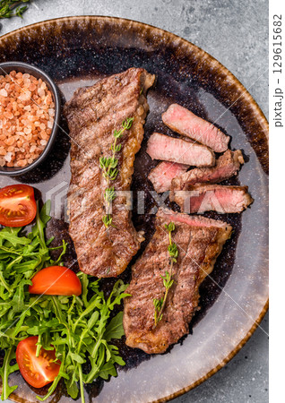 BBQ Grilled skirt or machete Steak, beef meat on a plate with salad. grey background. top view BBQ Grilled skirt or machete Steak, beef meat on a plate with salad. grey background. top view 129615682