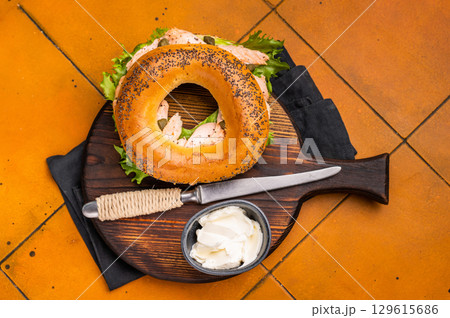 Breakfast Bagel with smoked salmon, lettuce and cream cheese on a wooden board. orange background. top view Breakfast Bagel with smoked salmon, lettuce and cream cheese on a wooden board. orange background. top view 129615686