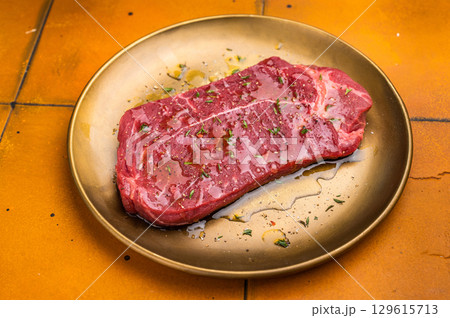 Marinated with olive oil and herbs Raw top sirloin or rump beef steak. orange background. top view 129615713