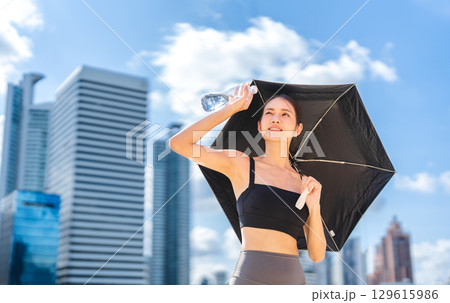 Asian sport woman holding umbrella and water pet bottle prevention from and thirsty heat stroke 129615986