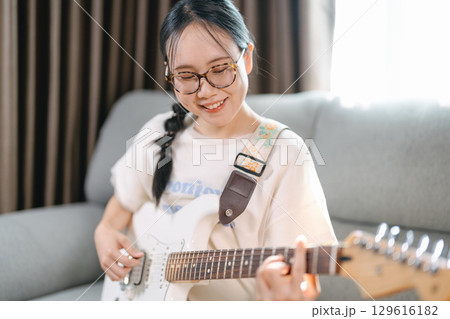 Young adult asian woman playing electric guitar music enjoy creativity hobby with musical instruments at home Young adult asian woman playing electric guitar music enjoy creativity hobby with musical instruments at home 129616182