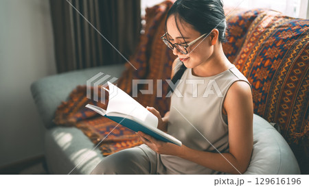Beautiful young adult asian woman wearing eyeglasses reading book on sofa relax hobby routines Beautiful young adult asian woman wearing eyeglasses reading book on sofa relax hobby routines 129616196