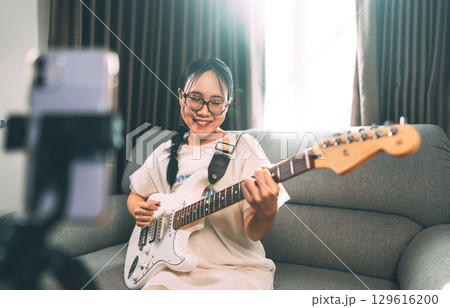 Young asian woman playing guitar live on social media Gen z content creator at home studio 129616200