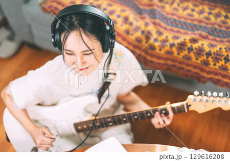 Young asian woman composer playing electric guitar wearing headphones 129616208