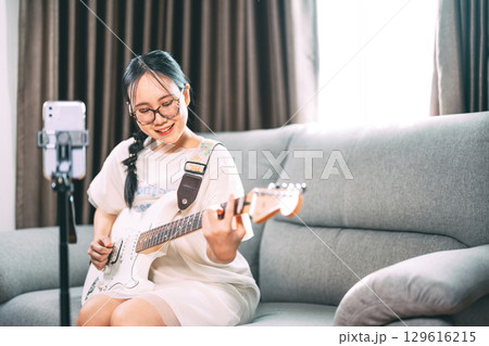 Young asian woman playing electric guitar live on social media content creator at home studio 129616215