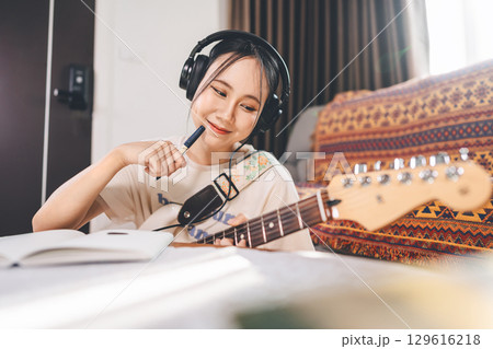 Young asian woman composer playing electric guitar wearing headphones 129616218