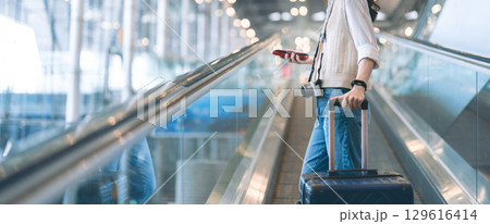 Standing passenger woman to transit with travel luggage and camera at international airport Standing passenger woman to transit with travel luggage and camera at international airport 129616414
