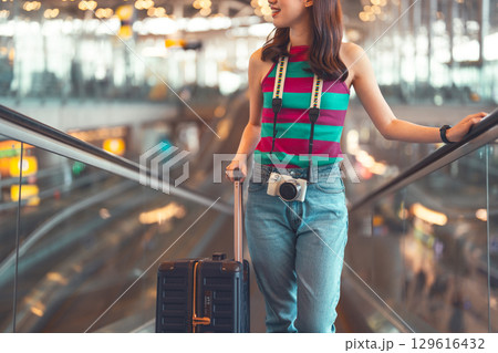 Standing passenger woman to transit with travel luggage and camera at international airport Standing passenger woman to transit with travel luggage and camera at international airport 129616432