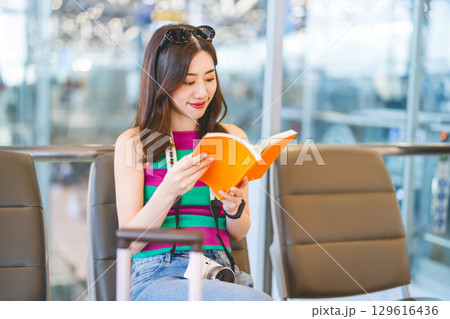 Woman reading a book at international airport terminal for waiting departure time. Woman reading a book at international airport terminal for waiting departure time. 129616436