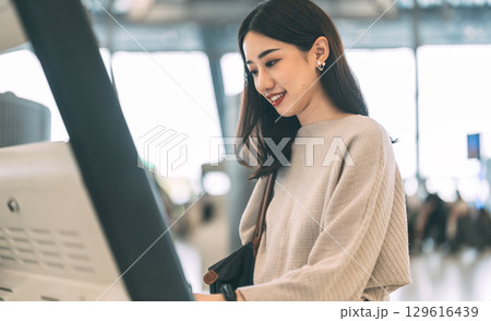 Woman passenger with travel luggage Using self service check kiosk machine at airport terminal Woman passenger with travel luggage Using self service check kiosk machine at airport terminal 129616439