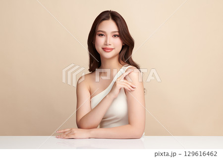 A beautiful young Asian woman with clean, fresh skin against a beige background. Skincare, facial treatment, cosmetology, beauty, and spa. An elegant portrait of an Asian woman. 129616462