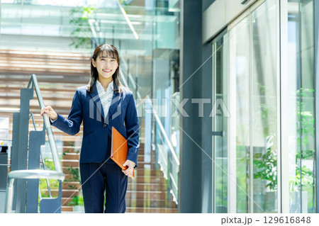 ファイルを持って歩くスーツ姿の女性 129616848