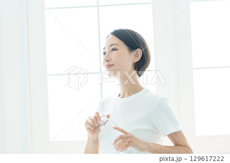 水が入ったウォーターボトルを持ち水分補給をする若い女性 水が入ったウォーターボトルを持ち水分補給をする若い女性 129617222