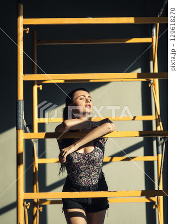 A brave girl stands near a scaffolding in a sporty style A brave girl stands near a scaffolding in a sporty style 129618270