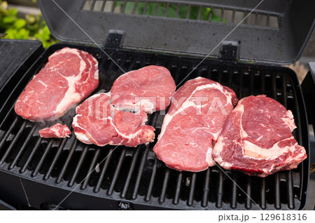 Four raw steaks on outdoor gas grill for summer barbecue cooking 129618316
