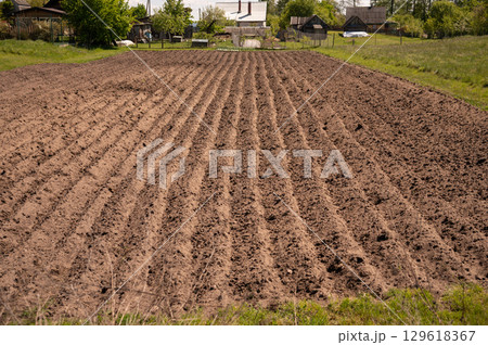 Freshly plowed field in rural countryside with green surroundings and blue sky 129618367