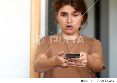 a young woman indoor, looking surprised at her phone. The photo, a powerful concept of bad news or a shocking message, is perfect for a technology or lifestyle-related theme a young woman indoor, looking surprised at her phone. The photo, a powerful concept of bad news or a shocking message, is perfect for a technology or lifestyle-related theme 129618385