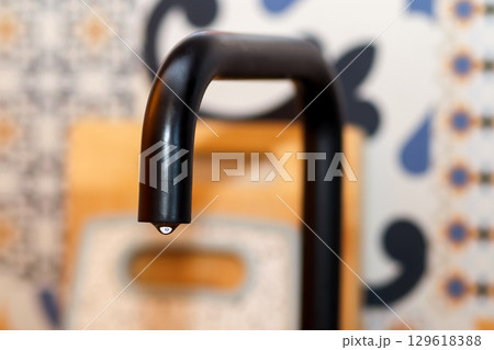 a single water drop falling from a sleek, black kitchen faucet. The photo is a powerful concept of a bank or money-related theme, with a focus on how to save water and energy 129618388