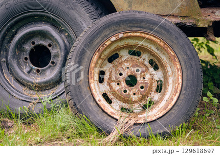 Rusty and worn vehicle wheels resting in tall grass at an abandoned location in daylight 129618697