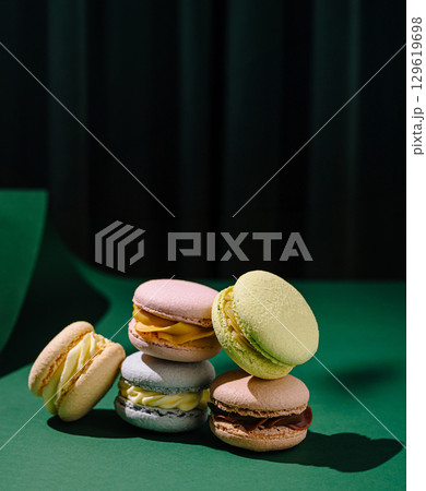 Colorful macarons stacked on a green surface with a dark backdrop 129619698