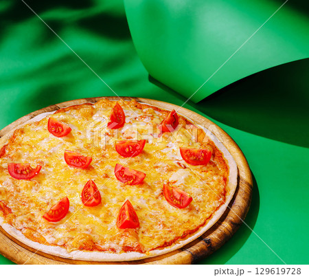Freshly baked pizza topped with sliced tomatoes on a vibrant surface 129619728