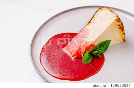 Delicious slice of cheesecake with raspberry sauce and mint garnish on a plate 129620027