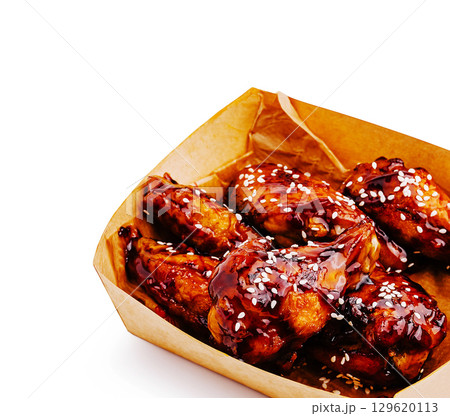 Crispy chicken wings topped with savory sauce and sesame seeds served in a box 129620113