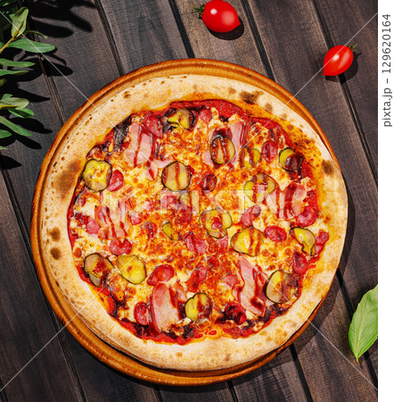 Deliciously baked pizza with toppings on a wooden table in bright sunlight 129620164