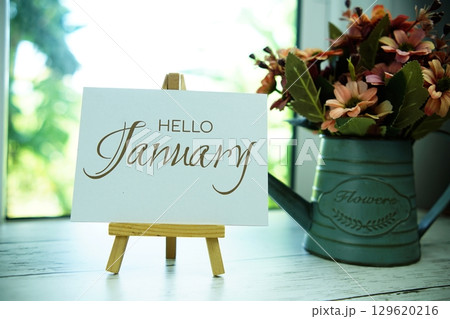 Hello January text on paper card with easel and alarm clock in the window background 129620216