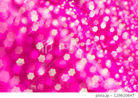 Defocused pink glitter background with star-shaped bokeh. A macro photo of water drops on a petunia flower petal, made with a nozzle on a star-shaped lens. Hexagon bokeh blur lens. 129620647