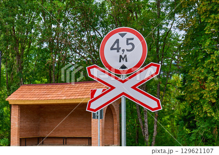 A railroad crossing warning sign stands by a bus stop in a wooded area during daylight A railroad crossing warning sign stands by a bus stop in a wooded area during daylight 129621107