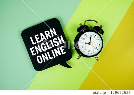 Learn English Online text on speech bubble with alarm clock top view on green and yellow geometric background 129622687
