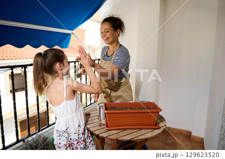 Mother and Daughter Gardening Together on a Sunny Balcony 129623520