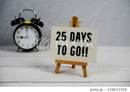 25 Days To Go! text with easel and alarm clock on wooden background 25 Days To Go! text with easel and alarm clock on wooden background 129623569