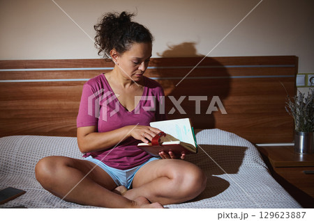 Woman Sitting on Bed Reading and Highlighting a Notebook in a Calm Atmosphere Woman Sitting on Bed Reading and Highlighting a Notebook in a Calm Atmosphere 129623887