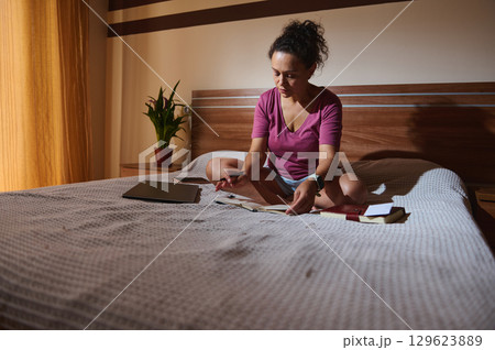 Woman Studying on Bed with Books and Device in Calm Room 129623889