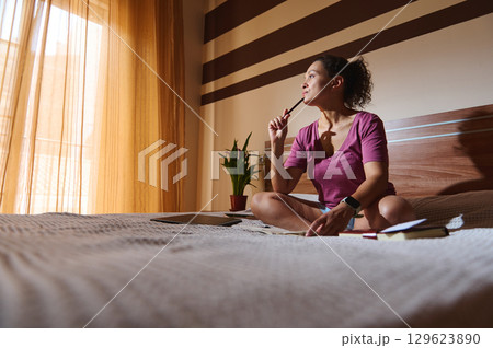 Woman Deep in Thought Sitting on Bed in a Sunlit Room Woman Deep in Thought Sitting on Bed in a Sunlit Room 129623890