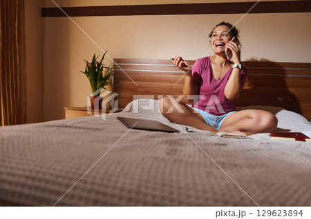 Young Woman Enjoying a Phone Conversation While Relaxing on Her Bed Young Woman Enjoying a Phone Conversation While Relaxing on Her Bed 129623894