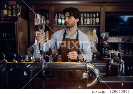 Brewer man brewer is carefully pouring beer into a glass Brewer man brewer is carefully pouring beer into a glass 129623992