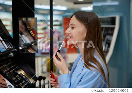 A woman is applying a vibrant shade of lipstick in a cosmetics store A woman is applying a vibrant shade of lipstick in a cosmetics store 129624061
