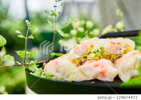 Fresh spring rolls served on a decorative tray surrounded by greenery in a vibrant outdoor setting Fresh spring rolls served on a decorative tray surrounded by greenery in a vibrant outdoor setting 129624431