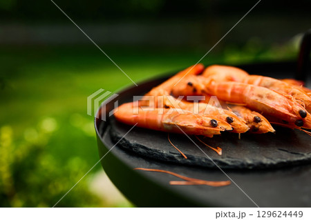 Grilled shrimp on a black grill plate surrounded by green grass in a sunny outdoor setting Grilled shrimp on a black grill plate surrounded by green grass in a sunny outdoor setting 129624449