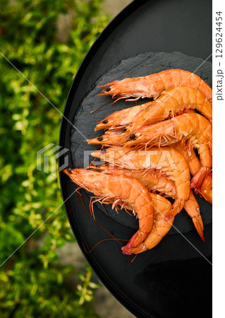 Grilled shrimp on a black grill plate surrounded by green grass in a sunny outdoor setting Grilled shrimp on a black grill plate surrounded by green grass in a sunny outdoor setting 129624454