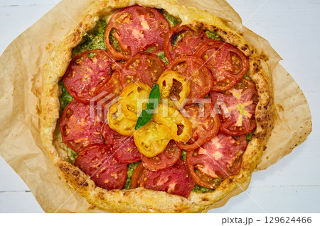 Freshly baked tomato galette on parchment paper served on a rustic wooden table in a cozy kitchen setting 129624466
